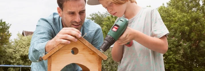 Eine Person baut mit Kind ein Vogelhaus mit einem Akkuschrauber